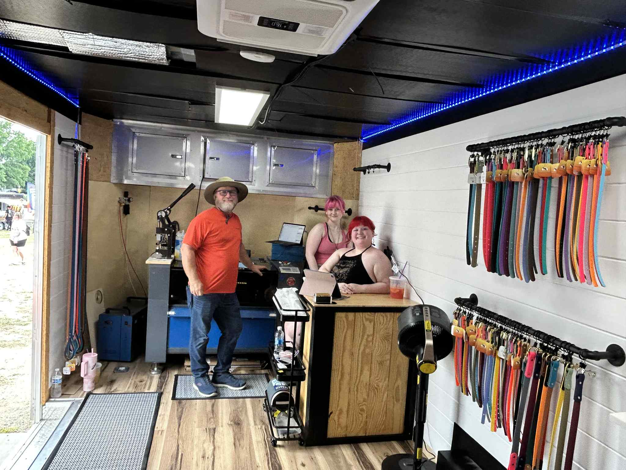 People inside The Leash Lounge trailer with various biothane dog collars and equipment.