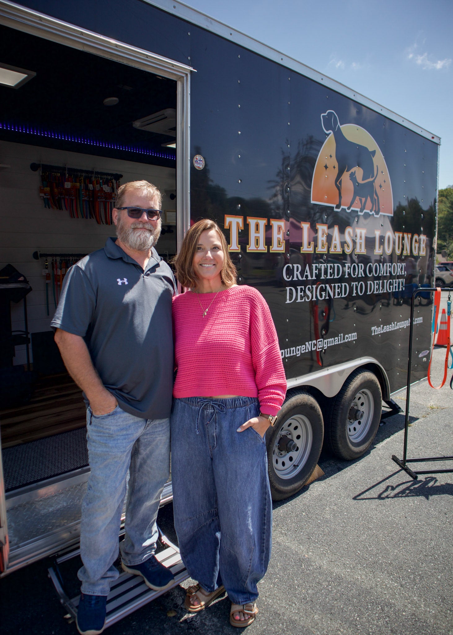 Two people (owners) standing in front of a trailer with 'The Leash Lounge' branding.